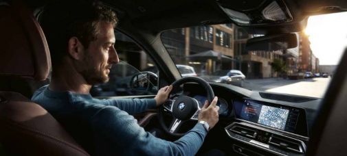 Mann fährt in einem BMW durch eine Stadt und blickt auf das Display in der Mittelkonsole