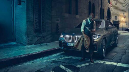 Mann steht in dunkler Nebenstraße mit Zeitung in der Hand vor seinem BMW