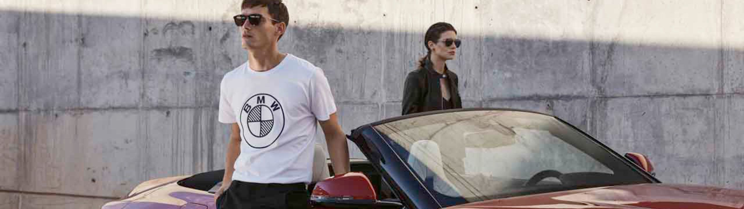 junger Mann mit weißem T-Shirt mi schwarzem BMW Logo steht vor einem roten BMW Z4