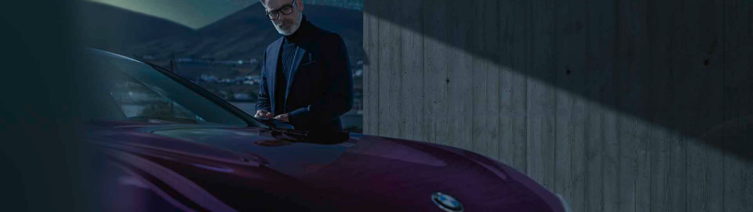 Gut gekleideter Mann mit weißem Bart steht in Dunkelheit neben lilafarbenen BMW 
