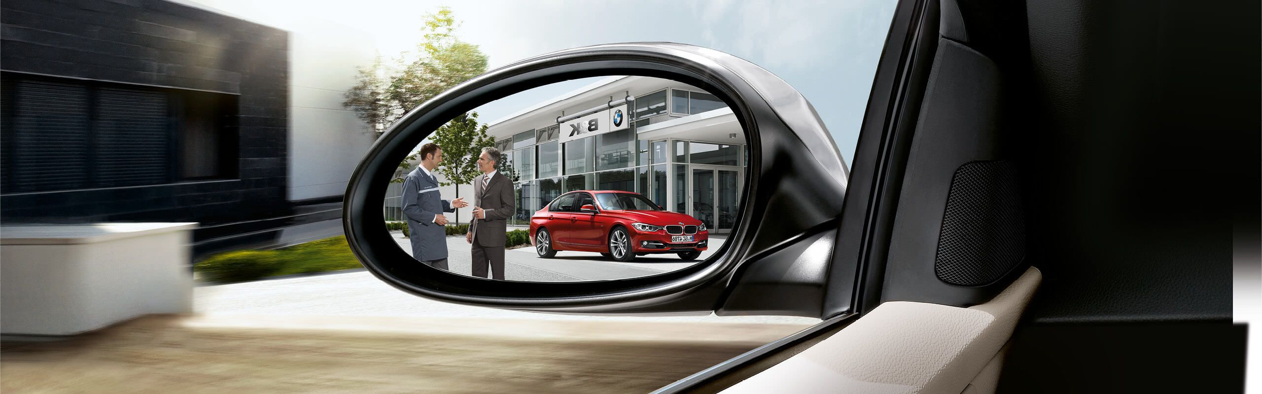 Zwei Männer stehen vor B&K Autohaus mit einem roten BMW