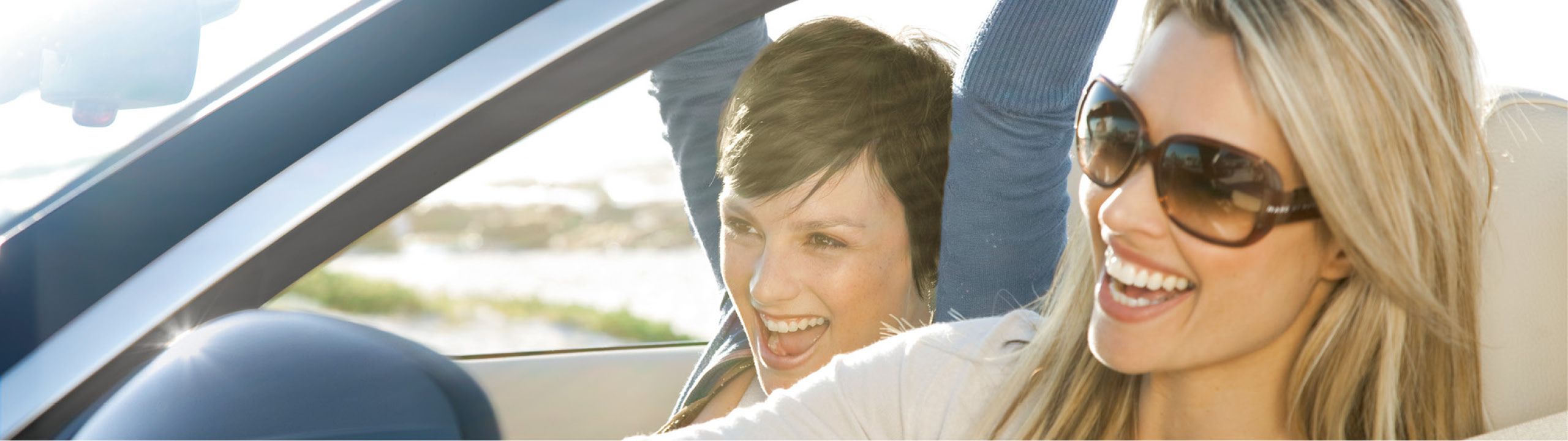 Zwei Frauen sitzen im Cabrio und lachen